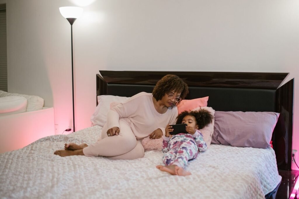 Mother and daughter in pajamas enjoy cozy time together watching tablet in bed.
