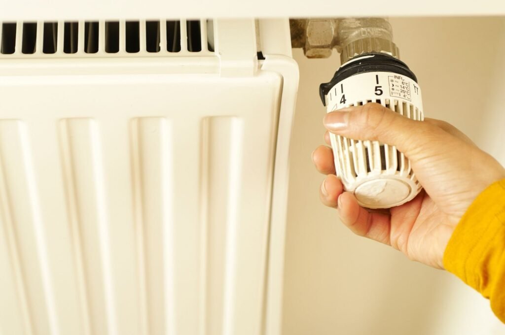 Photo by BOOM 💥 Photography Close-up of hand adjusting radiator thermostat to control home heating temperature.