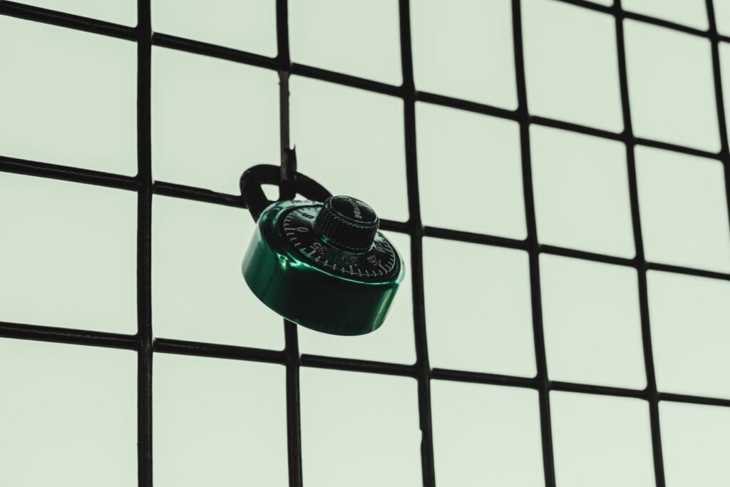 A green combination lock is attached to a wire fence grid, symbolizing security.
