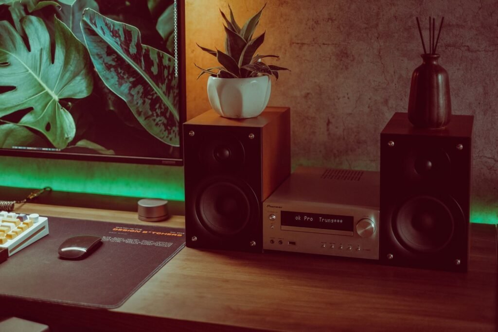 A cozy vintage desk setup featuring speakers, plants, and audio equipment with a warm ambiance.