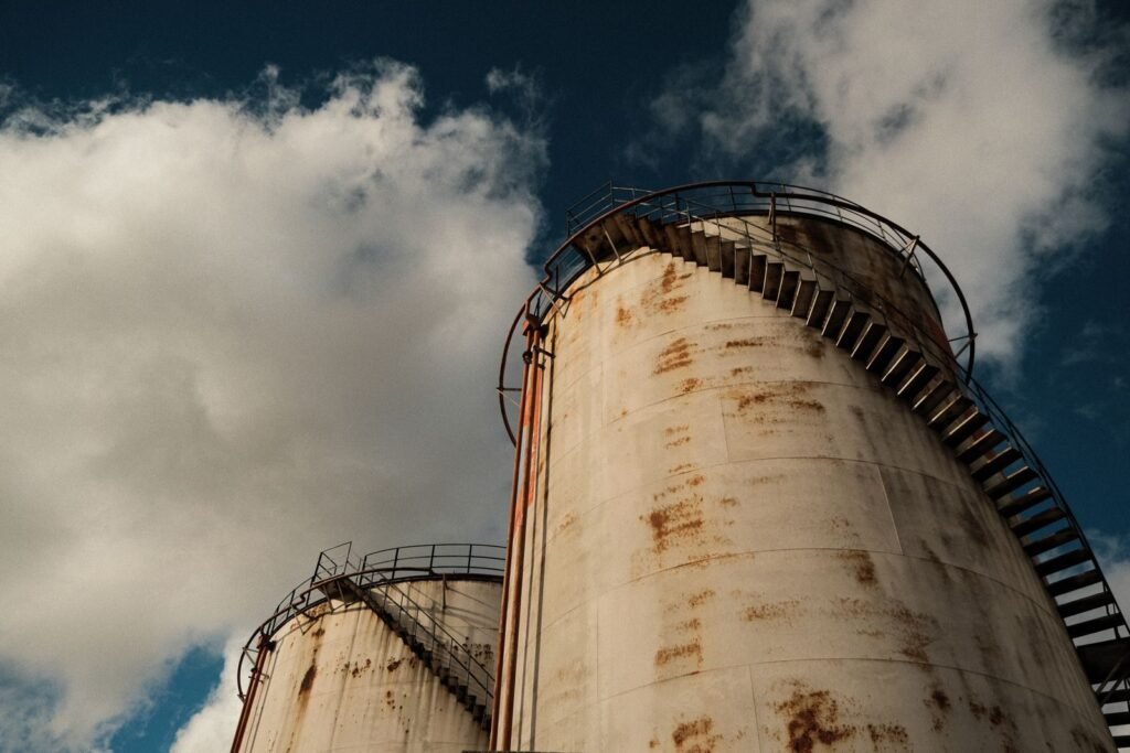 Vintage industrial silos with rust patterns against a cloudy blue sky.