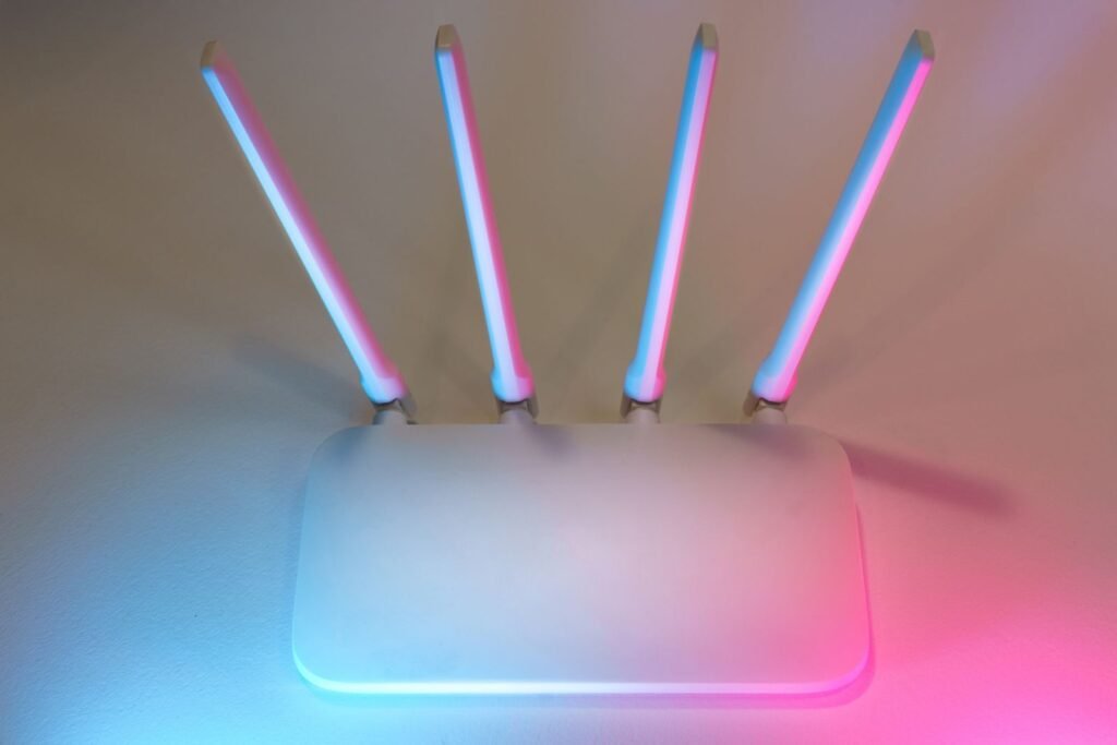 Photo by Jakub Zerdzicki Sleek white wireless router with four antennas emitting soft blue and pink light.