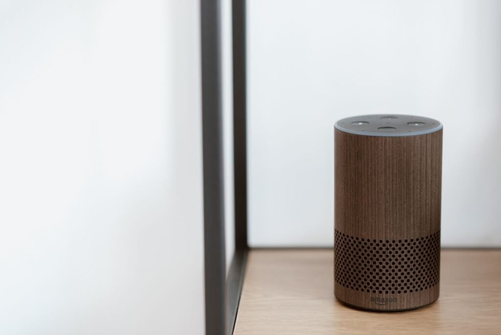 Photo by Anete Lusina A sleek, modern smart speaker displayed on a wooden shelf in a minimalist room setting.