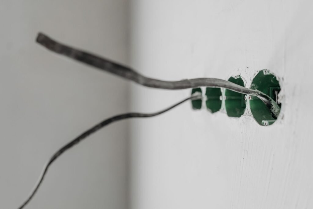 Photo by Pavel Danilyuk Unfinished electrical outlet installation with exposed wires on a white wall.