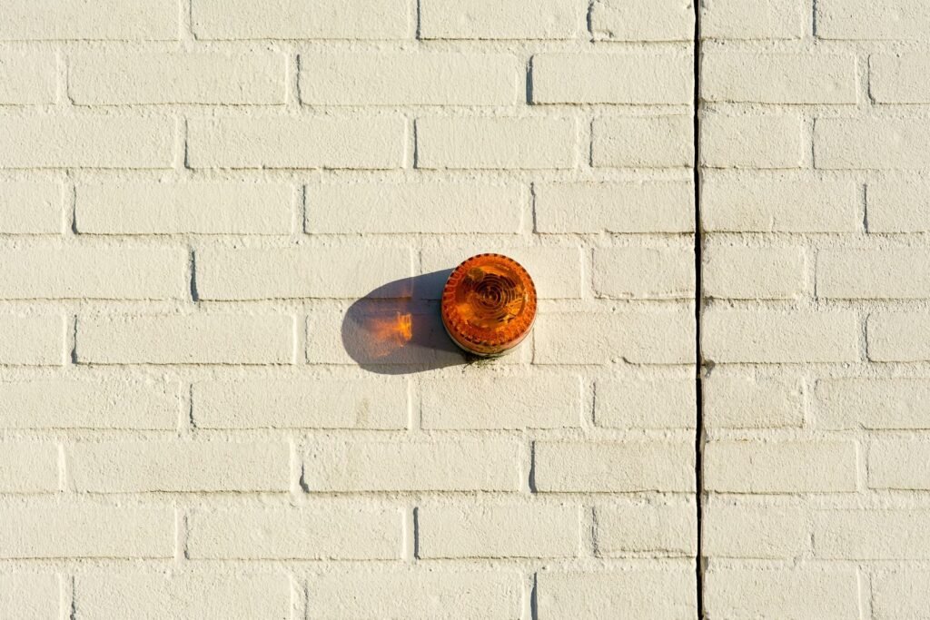 An orange warning light mounted on a white painted brick wall casting a shadow.