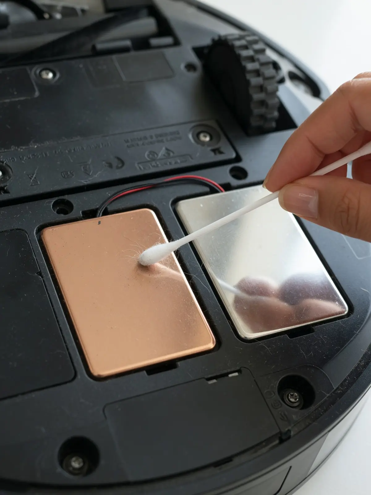 Person using a cotton swab to clean the metal charging contacts underneath a Shark robot vacuum to fix charging issues